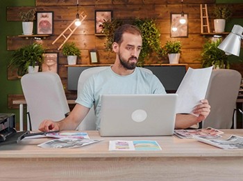 Young Designer Looking At A It In His Hand While Sitting.